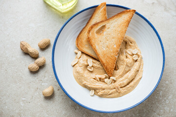 Blue and white plate with peanut butter and toasts, horizontal shot on a beige stone background, elevated view