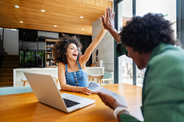 A young couple of African descent is sitting in a modern living room, both smiling and enjoying...