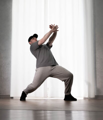 Dance in motion, pose of a man in hip-hop style clothes. Sports dancing guy in training poses. Dance training at home.