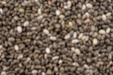 Numerous dried or dehydrated chia seeds spread evenly.blurred image