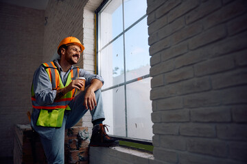 Happy worker having  cup of coffee while taking  break at construction site.
