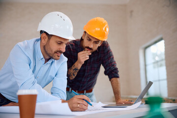 Smiling architect and construction worker analyzing blueprints during house remodeling.