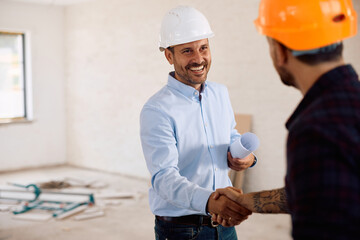 Happy architect and construction worker shaking hands during house remodeling project.