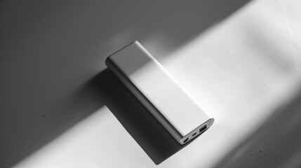 External battery pack creates dramatic shadow on white surface, ideal for charging devices while traveling