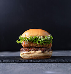 Gourmet chicken burger with cheese and veggies. Juicy delicious hamburger on darkmood picture for restaurant decoration, poster.
