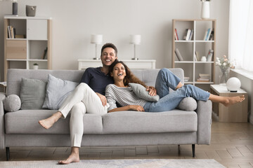Cheerful couple spend leisure time at home, relaxing on cozy sofa, looking at camera, pose,...