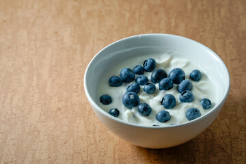 White bowl of yoghurt with blueberries isolated on brown