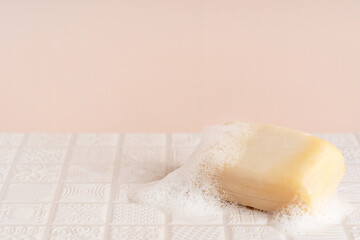 Organic antibacterial wet natural handmade square soap bar with white foam and bubbles on bathroom tile on light beige background with copy space used in shower for healthy body hygiene and skin care