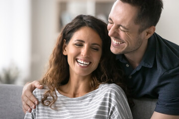 Close up beautiful overjoyed Latin couple talking, laughing, spend time together at home. Cheerful husband hugs his beloved beautiful wife, joking, giggling, feel carefree and happy. Relations, love