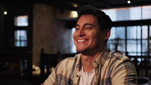 Portrait of young hispanic man in coworking space. Dark haired guy smiles pointing a finger at the other person