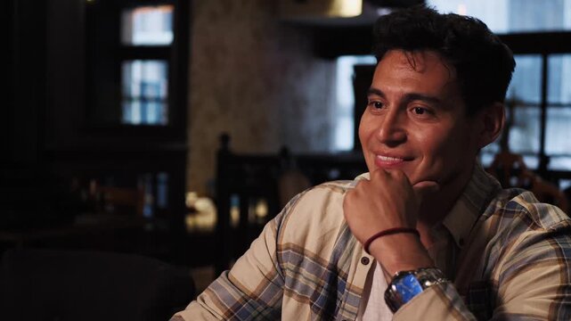 Portrait of young hispanic man in coworking space. Dark haired guy smiles looks forward smiling