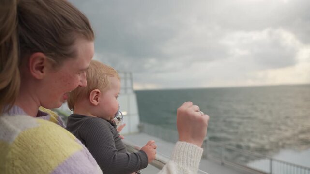 Mother Waves Towards The Sea While Baby Is Sucking On Pacifier