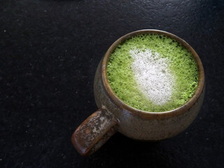Cup of green tea matcha latte savory milk foam on the dark background closeup