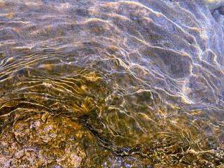 Stone in the clear transparent water with sun glare