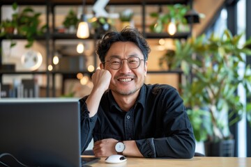 Obraz premium A Japanese man in an office, smiling with arms behind head, relaxed, sitting at a desk with a laptop, business casual attire, modern office background