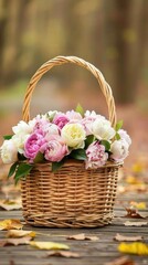 A woven basket filled with vibrant pink and white peonies rests on a colorful blanket of fallen autumn leaves in a picturesque forest