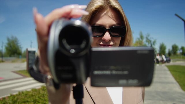 A young woman is filming a video outdoors using a camcorder on a bright sunny day, pov video of filming backstage, retro vintage mini dv camera.