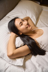Fototapeta premium Smiling dreaming woman of Asian ethnicity lying in comfortable bed