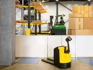 Electric pallet jack in warehouse. Equipment for unloading. Pallet jack in industrial building. Warehouse with cardboard boxes. Pallet jack for loading pallets into machine. Storage area