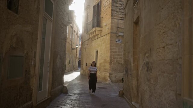 A young hispanic woman smiling and walking through the picturesque stone alleyways of lecce in puglia, italy, radiating joy amidst historic buildings.