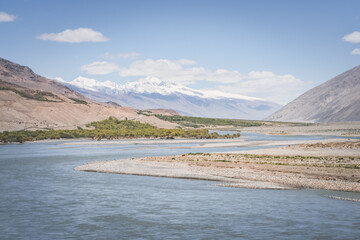 Pyanj River flows in Wakhan Valley among rocky high mountains against snow-capped peaks and glaciers in Tajikistan's Tien Shan mountains, landscape for background