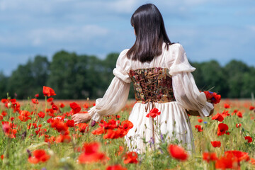 young medieval maid looks with her back to the camera over a field of flowers