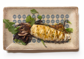 Bbq squid calamary on a rack and seasoned with lemon and salad on a rectangular plate