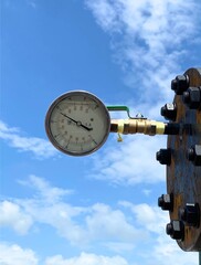 Fototapeta premium Close-up of an industrial pressure gauge attached to a pipeline against a clear blue sky. The image highlights precision measurement and monitoring in industrial processes.