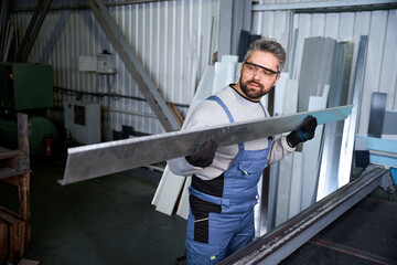 Employee of production workshop holds aluminum profile in his hands