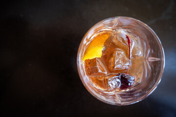 A glass of whiskey with a cherry on top and an orange slice inside. The drink is a traditional old fashioned manhattan.