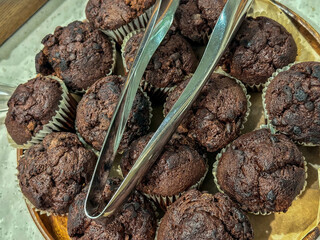 Platter full of chocolate chip muffins with tongs for selection