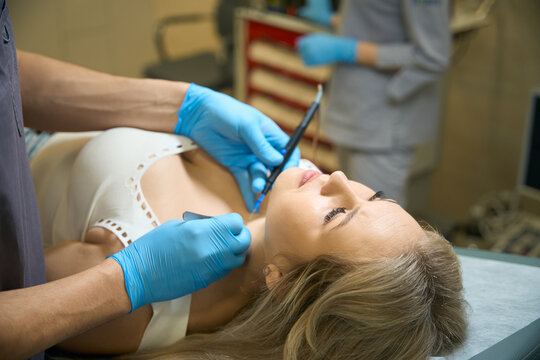 Doctor cauterizing mole on female patient neck with electric current