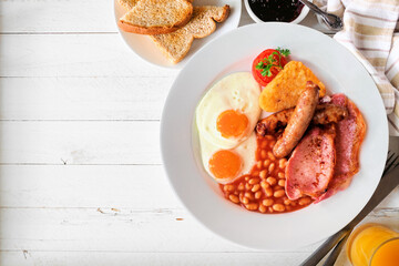 Full English breakfast with baked beans, bacon, eggs, sausage and hash browns. Above view table scene on a white wood background with copy space.