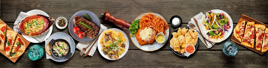 Table scene of various delicious foods. Above view on a dark wood banner background. Pastas,...