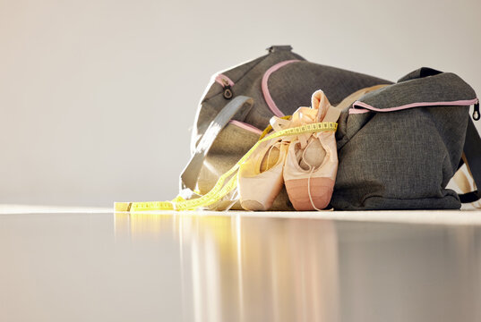 Closeup, isolated and ballet slippers on floor with exercise bag, measuring tape and lose weight for health. Zoom, dance and pointe shoes on ground with workout duffle, training progress and goals