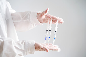 The doctor's hands in a white coat and gloves hold three syringes with medicine.