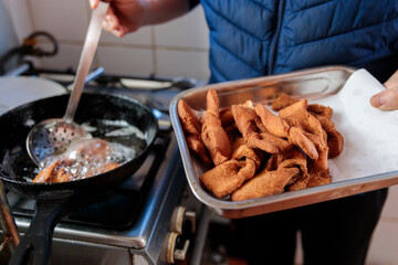 Unrecognizable latin man's hands deep-frying chilean sweet fried pastry calzones rotos in a pan in her domestic kitchen 