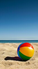 Obraz premium A colorful beach ball resting on the golden sand under a clear blue sky.