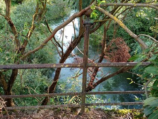 River landscape from the height of an old ruined concrete bridge with rusted metal railings.