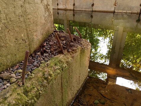 A large old concrete pillar near the reservoir, from the base of which rebar pins stick out. Industrial backgrounds and landscapes.