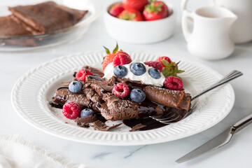 A plate of homemade chocolate crepes topped with whip cream and berries.