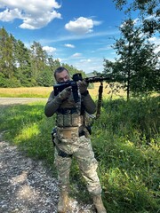 Fototapeta premium A soldier aiming a rifle. A soldier with a rifle in his hand standing in the forest. Dressed in camouflage.