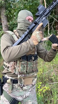 A soldier aiming a rifle.  A soldier with a rifle in his hand standing in the forest.  Dressed in camouflage.