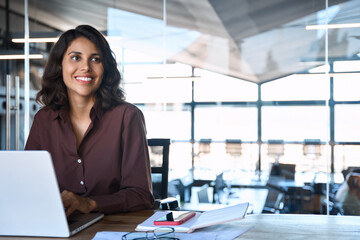 Portrait of smiling latin hispanic middle-aged business woman work on laptop computer in modern...