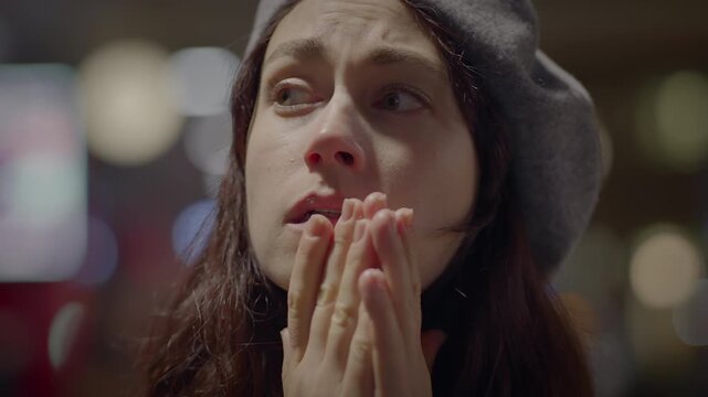 A woman wearing a beret is covering her nose and mouth with her hands in an emotional moment