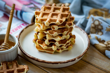 Dessert for breakfast: a stack of Viennese waffles on a white plate on a wooden table. Close-up.