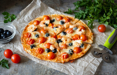 Italian dish: pizza with cherry tomatoes, shrimp, olives and mozzarella on a gray background. Slices of pizza margarita on parchment. Close-up.