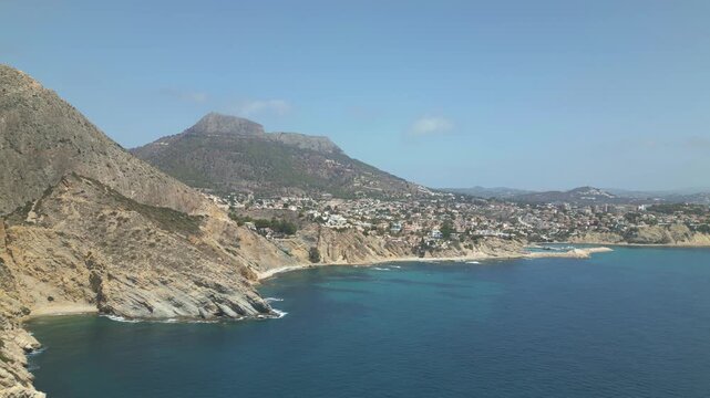 A beautiful blue ocean with a rocky shoreline and a mountain in the background. The sky is clear and the sun is shining. Calpe, alicante
