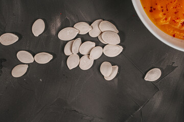 Pumpkin seeds with pumpkin puree soup on a gray, graphite background.