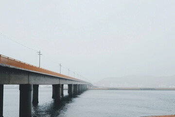 Long concrete bridge over calm water in foggy weather